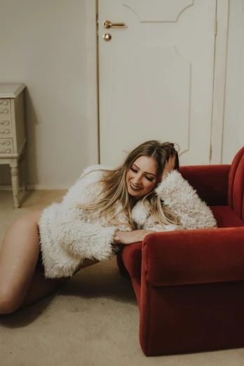 a woman laying on top of a red chair, an album cover, inspired by Elsa Bleda, trending on pexels, fur jacket, warm smile, sydney sweeney, in white room