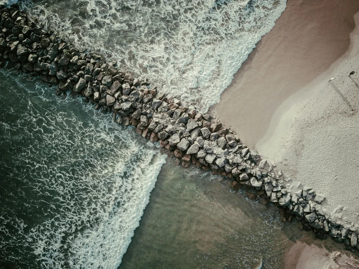 a group of rocks sitting on top of a beach next to the ocean, by Adam Marczyński, pexels contest winner, conceptual art, river flowing through a wall, close-up from above, bridge over the water, hyperdetailed photograph