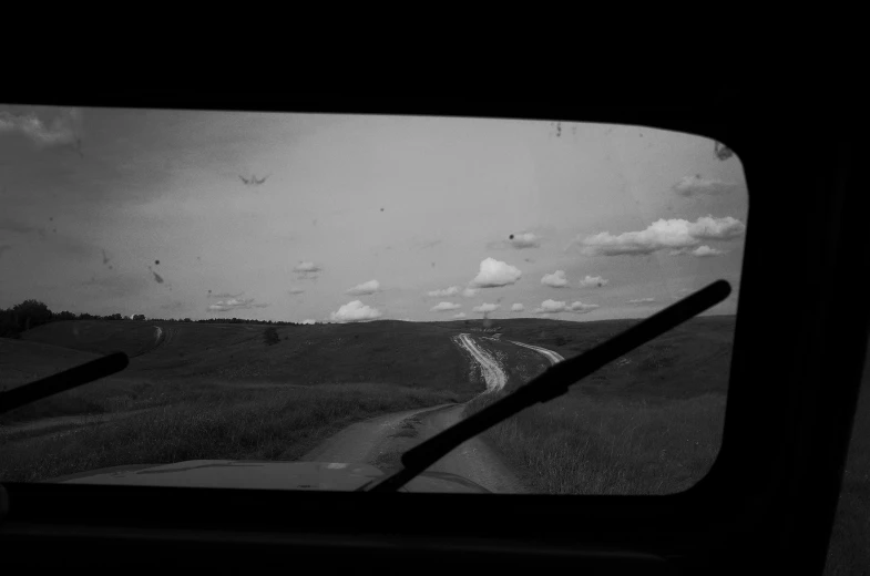 a black and white photo of a dirt road, inspired by Bert Hardy, unsplash, conceptual art, 1 9 7 0 s car window closeup, prairie in background, looking out open window, movie filmstill