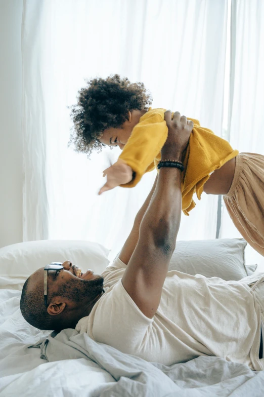 a man and a little girl laying on a bed, inspired by The Family Circus, pexels contest winner, black man, raising an arm, wearing a tee shirt and combats, high textured