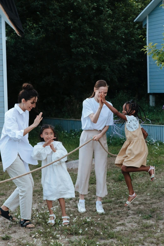 a group of people that are standing in the grass, wearing a white blouse, kids playing, wearing white suit, pulling strings