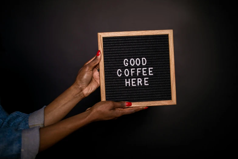 a woman holding a sign that says good coffee here, by Arabella Rankin, trending on unsplash, light box, 1 6 x 1 6, panel of black, ashteroth