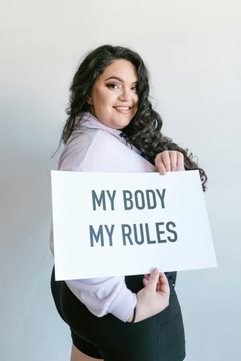 a woman holding a sign that says my body my rules, pexels contest winner, curvy build, kailee mandel, profile image, rebecca sugar