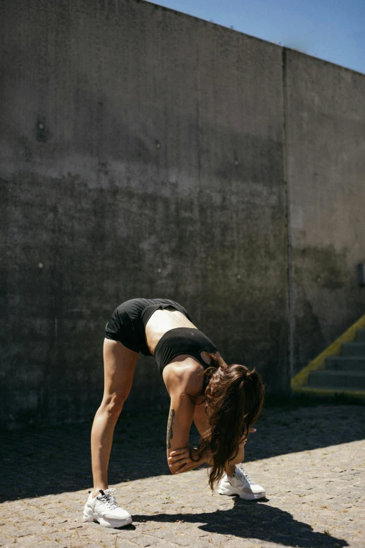 a woman doing a handstand in front of a wall, pexels contest winner, tight black tank top and shorts, vsco film grain, brunette fairy woman stretching, hunched shoulders