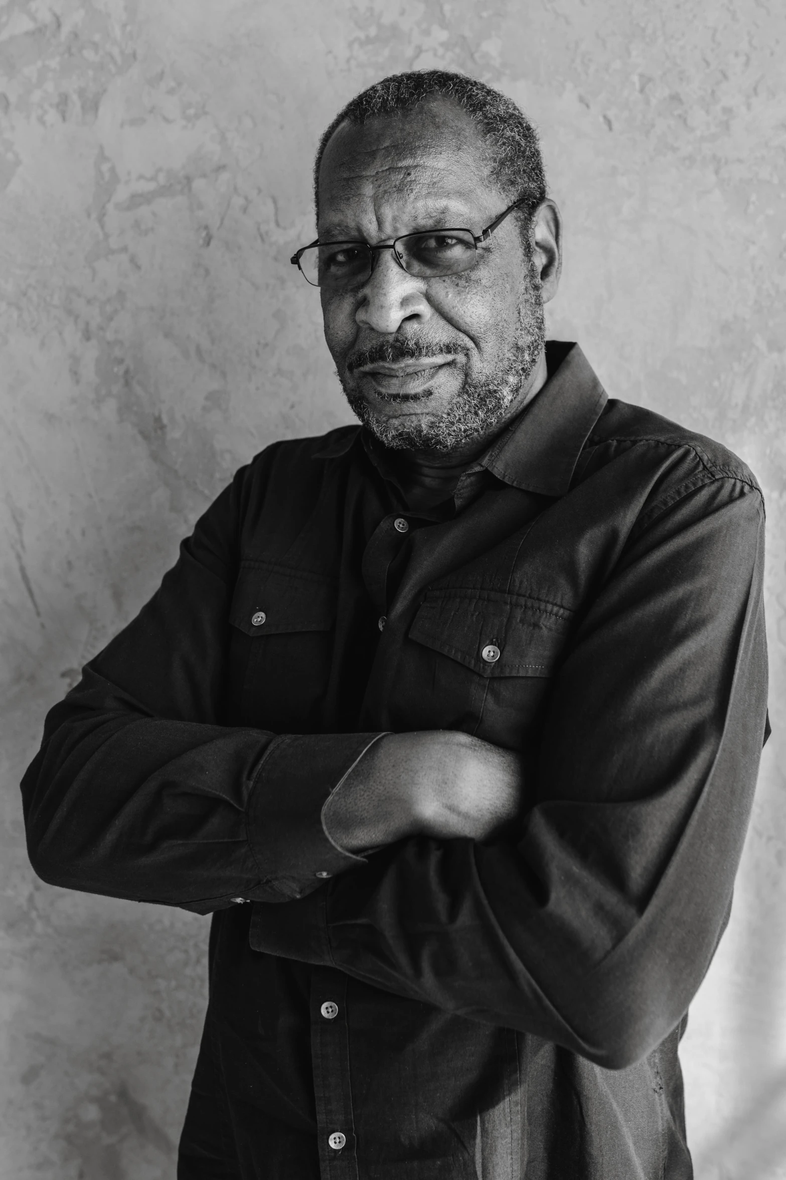 a black and white photo of a man with his arms crossed, inspired by Ismail Gulgee, anthony avon, portrait image, slightly smirking, george floyd