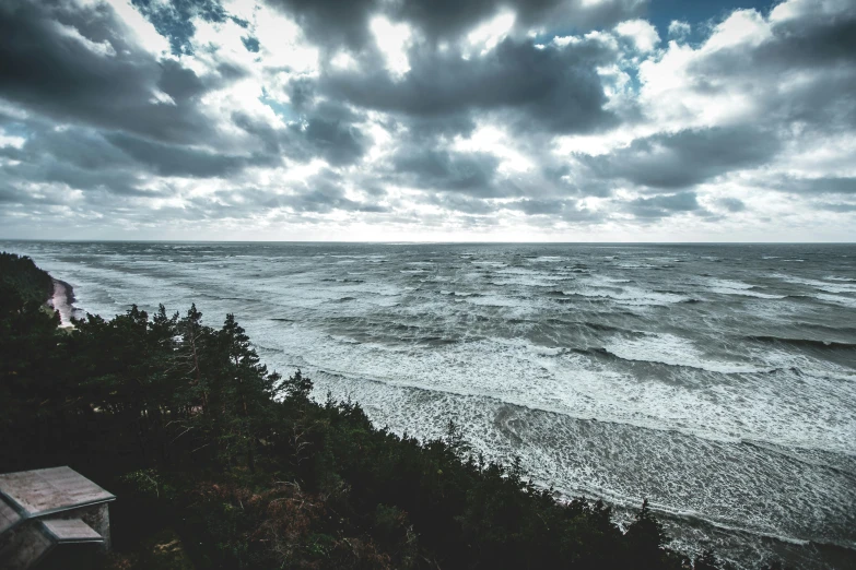 a bench sitting on top of a cliff next to the ocean, a picture, unsplash contest winner, surrealism, turbulent storm clouds, ominous! landscape of north bend, an eerie whirlpool, wide high angle view