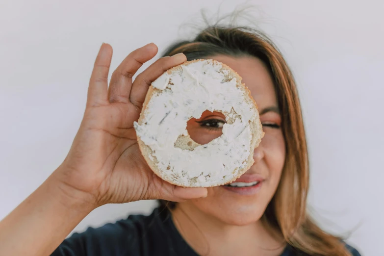 a woman holding a donut in front of her face, by Will Ellis, pexels contest winner, hurufiyya, cheeses, well preserved, avatar image, white around right eye