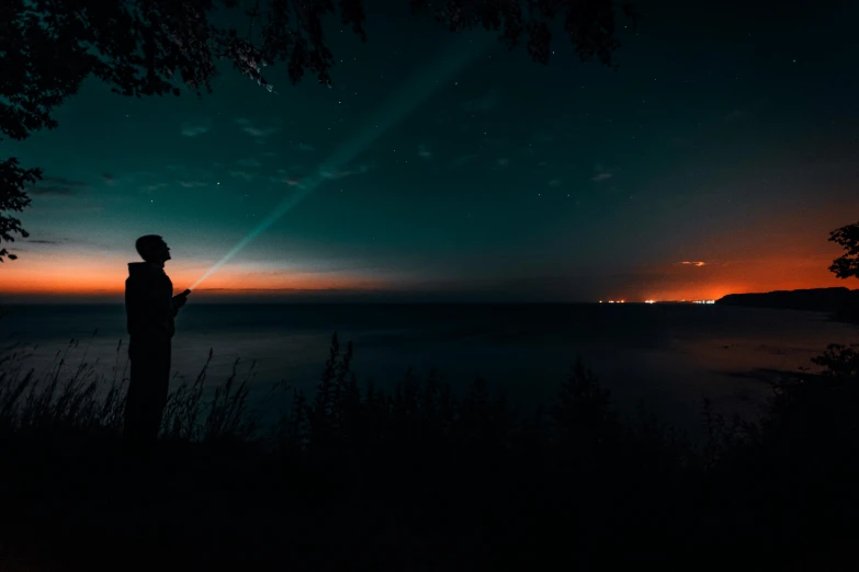 a person standing on top of a hill at night, pexels contest winner, gazing at the water, holding a torch, instagram picture, faded glow