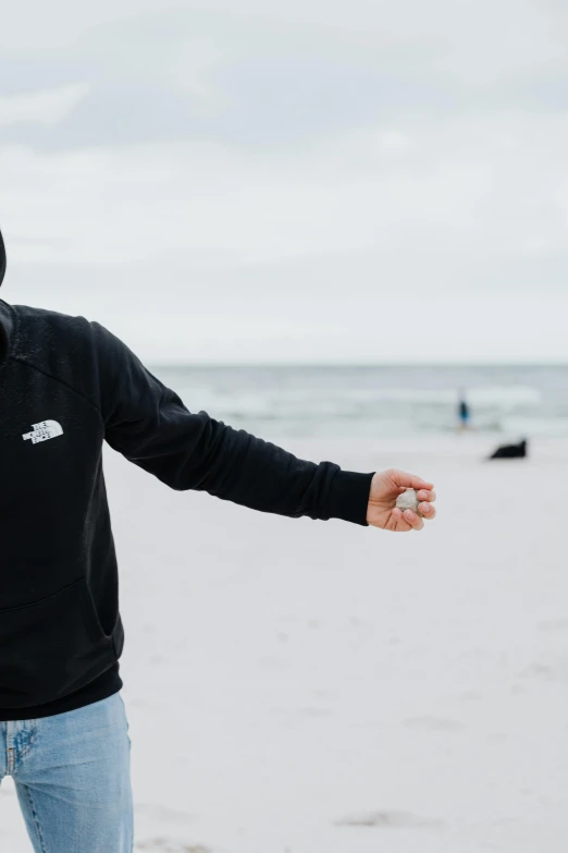 a man standing on top of a sandy beach, wearing a black hoodie, with pointing finger, unsplash transparent, snacks