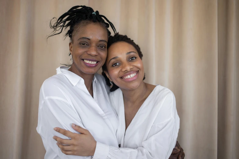 a couple of women standing next to each other, a portrait, light-brown skin, supportive, in front of white back drop, digital image