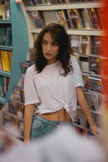 a woman standing in front of a book shelf, an album cover, inspired by Nan Goldin, trending on pexels, with ripped crop t - shirt, kiko mizuhara, at a mall, dressed in a white t-shirt