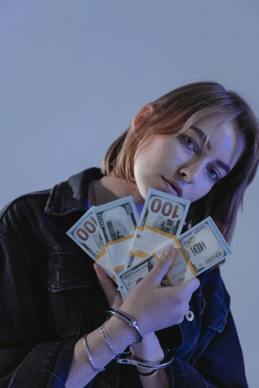 a woman holding a bunch of money in her hands, a colorized photo, inspired by Elsa Bleda, trending on unsplash, renaissance, portrait of max caulfield, twitch streamer, college, sadie sink