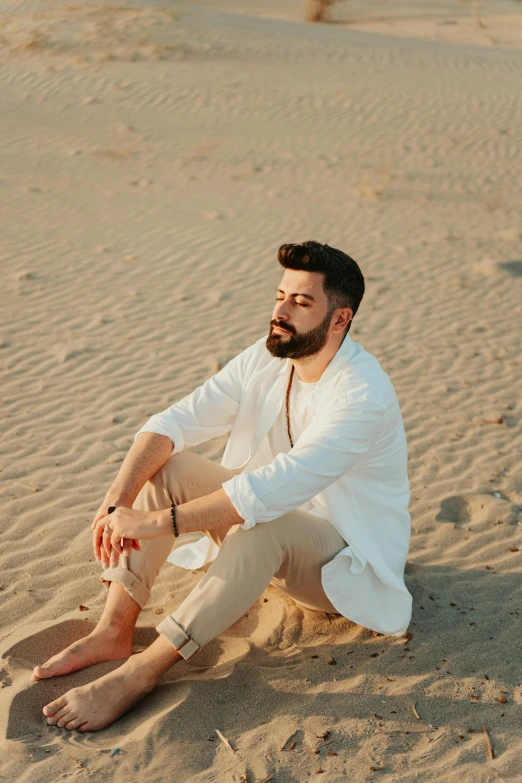 a man sitting on top of a sandy beach, an album cover, inspired by Amir Zand, pexels contest winner, renaissance, bearded beautiful man, wearing white shirt, stylish pose, sandy colors