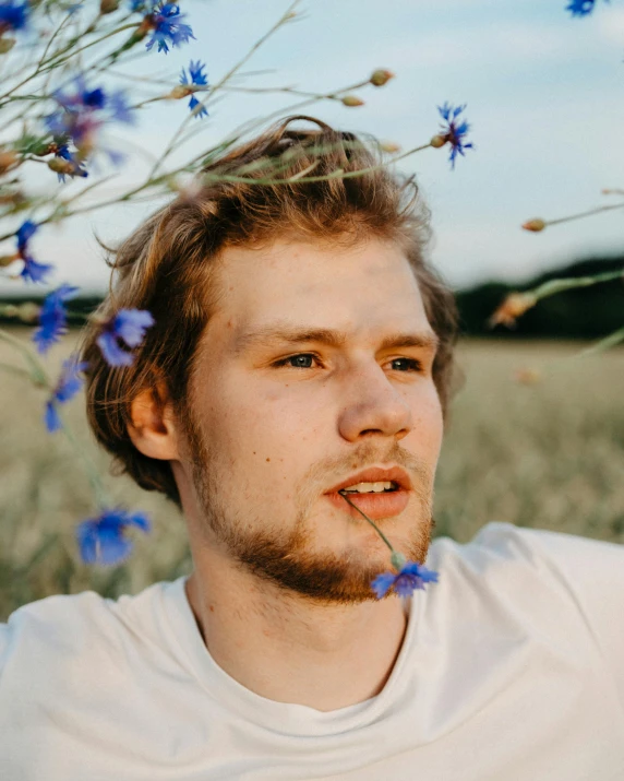 a man standing in a field of blue flowers, a colorized photo, by Attila Meszlenyi, trending on unsplash, romanticism, light brown hair blue eyes, yung lean, grinning lasciviously, non binary model