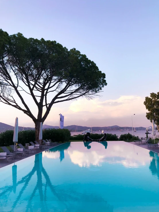 a swimming pool surrounded by lounge chairs and trees, pexels contest winner, cannes, sunset view, thumbnail, 8 k -