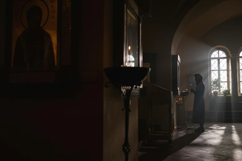a person standing in a dimly lit room, romanesque, cinematic movie still, in orthodox church, fan favorite, behind the scenes photo