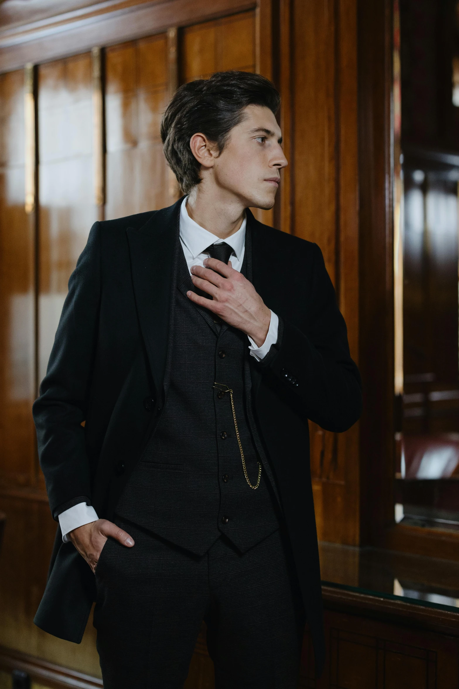 a man in a suit adjusting his tie, inspired by George Henry, renaissance, costumes from peaky blinders, delicate androgynous prince, standing in corner of room, model is wearing techtical vest