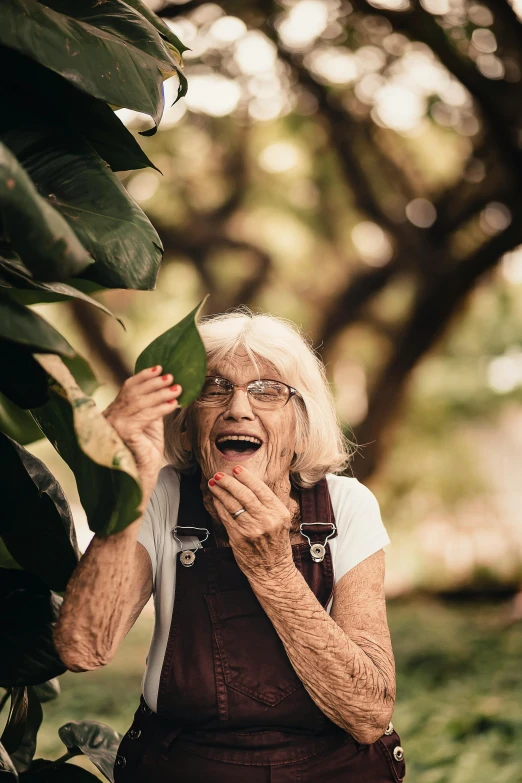 an older woman holding a leaf up to her face, an album cover, pexels contest winner, laughing hysterically, lush nature, old man, advanced technology