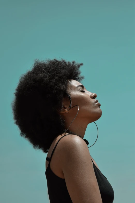 a woman standing in front of a blue wall, pexels contest winner, afrofuturism, black man with afro hair, cloudless sky, listening to godly music, focused on her neck