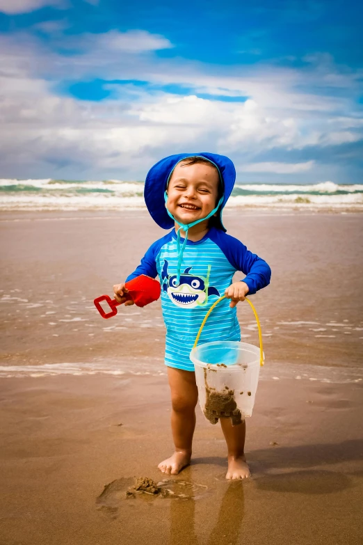 a little boy standing on top of a sandy beach, blue themed, drenched clothing, smiling, thumbnail