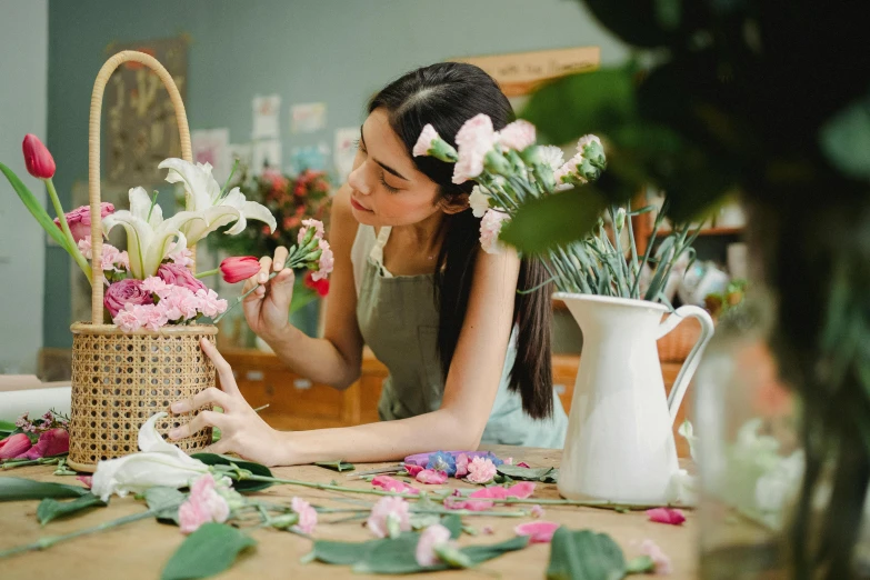 a woman arranging flowers in a basket on a table, pexels contest winner, arts and crafts movement, pink white and green, sydney hanson, jenna barton, mina petrovic