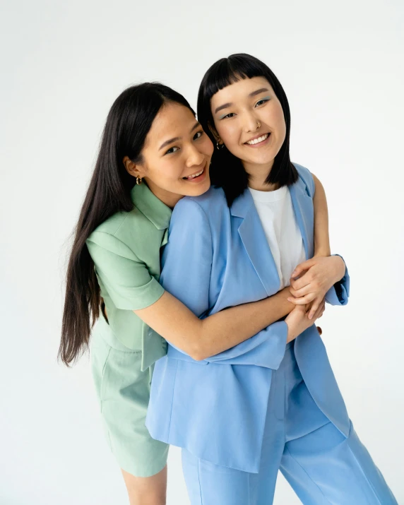 a couple of women standing next to each other, inspired by Wang Duo, trending on unsplash, dau-al-set, wearing a light blue suit, cuddling, colorful uniforms, set against a white background