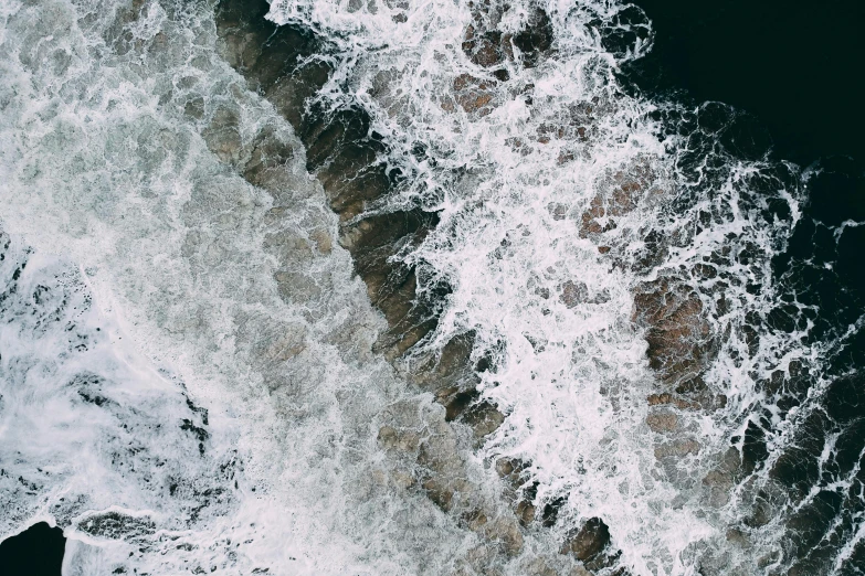 a person riding a surfboard on top of a wave, trending on unsplash, water texture, rocky shore, looking down from above, dark and white