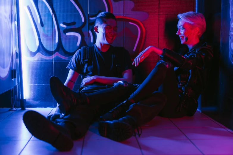 two men sitting next to each other in a room, unsplash, graffiti, a 1980s goth nightclub in soho, lesbians, sitting on the ground, smiling at each other