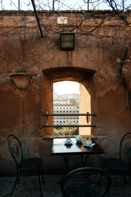 a table and chairs in front of a brick wall, by Riad Beyrouti, trending on unsplash, neoclassicism, drinking tea, view from inside, colosseo, roof garden