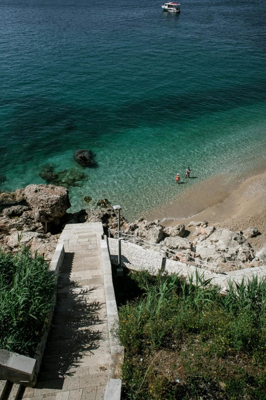 a wooden bench sitting on top of a beach next to a body of water, renaissance, steps leading down, croatian coastline, slide show, top - down photograph