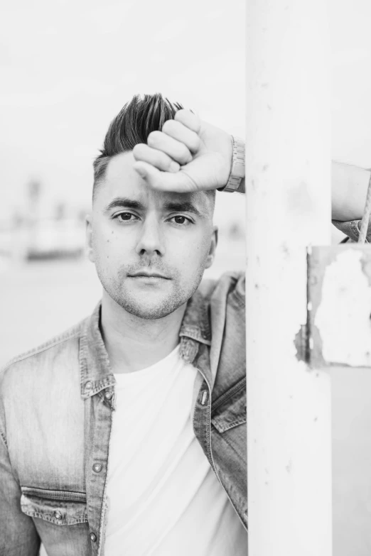 a black and white photo of a man leaning against a pole, inspired by Kyle Lambert, spikey hair, in front of white back drop, irish youtuber, classified