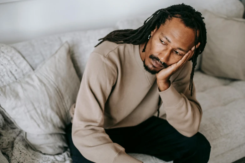 a man with dreadlocks sitting on a couch, a cartoon, trending on pexels, romanticism, grieving, he is wearing a brown sweater, man in his 40s, someone sits in bed