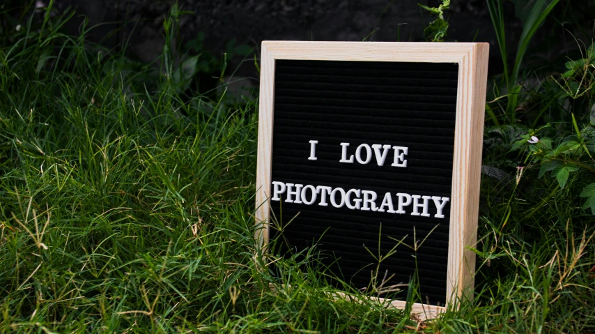 a sign that says i love photography sitting in the grass, a picture, unsplash, with a black background, professional product photo, sign, photograph”