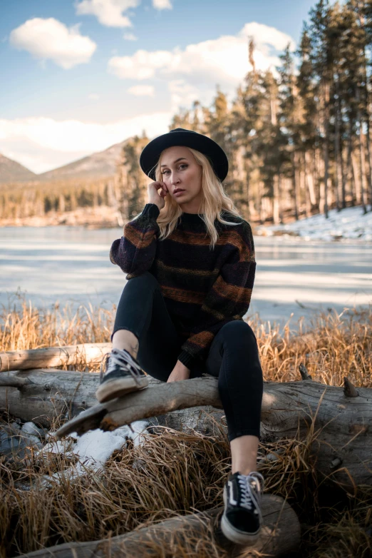 a woman sitting on a log next to a lake, a portrait, trending on pexels, winter vibes, fullbody photo, blonde, college