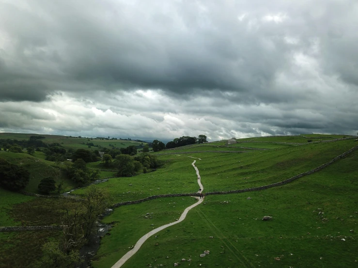 a dirt road running through a lush green field, by Kev Walker, pexels contest winner, land art, limestone, dark cloudy sky, overview, shap