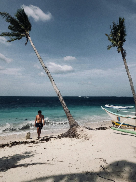 a man walking on a beach next to a boat, by Robbie Trevino, coconut trees, white beaches, trending on vsco, very accurate photo