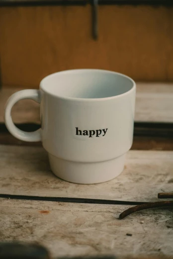 a white cup sitting on top of a wooden table, inspired by Harvey Quaytman, unsplash, happy smiling, hidden message, front closeup, multilayer