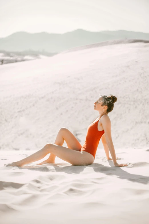 a woman sitting on top of a sandy beach, trending on pexels, red body suit, smooth white surroundings, sun lighting, profile image