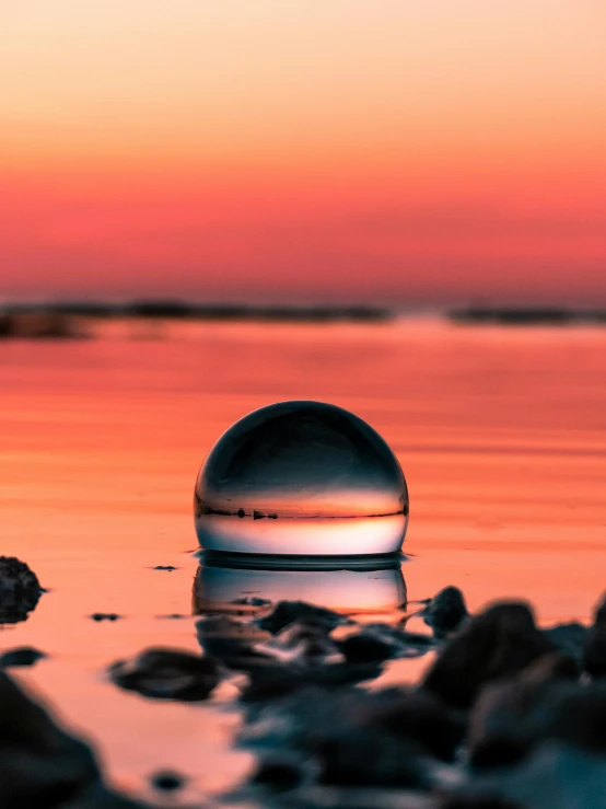 a glass ball sitting on top of a body of water, during sunset, 8k award-winning photograph, gravitational lens, high-quality photo