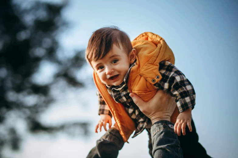 a man holding a small child in his arms, pexels contest winner, wearing a flying jacket, climber, brown, happy kid