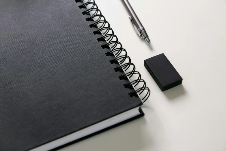 a notebook, pen, and eraser on a table, a drawing, inspired by artist, unsplash, black matte finish, sparse detail, product view, anthracite