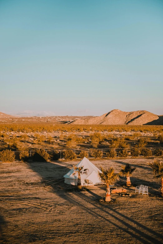 a white tent sitting in the middle of a desert, lush oasis, in the golden hour, overview, exterior