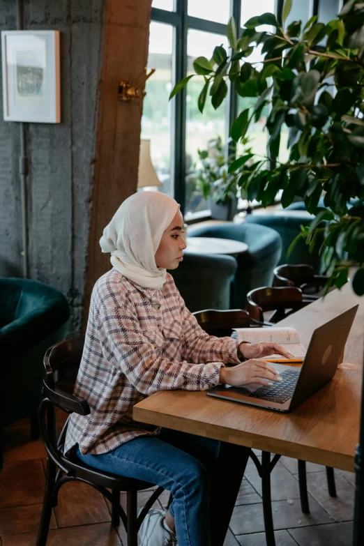 a woman sitting at a table with a laptop, by Ismail Acar, trending on unsplash, hurufiyya, white hijab, full-body, high quality screenshot, small