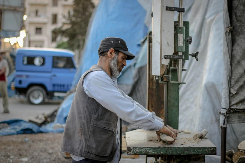 a man that is standing in front of a machine, by Arthur Sarkissian, pexels contest winner, real life photo of a syrian man, holding a wood piece, saw, holding a baguette