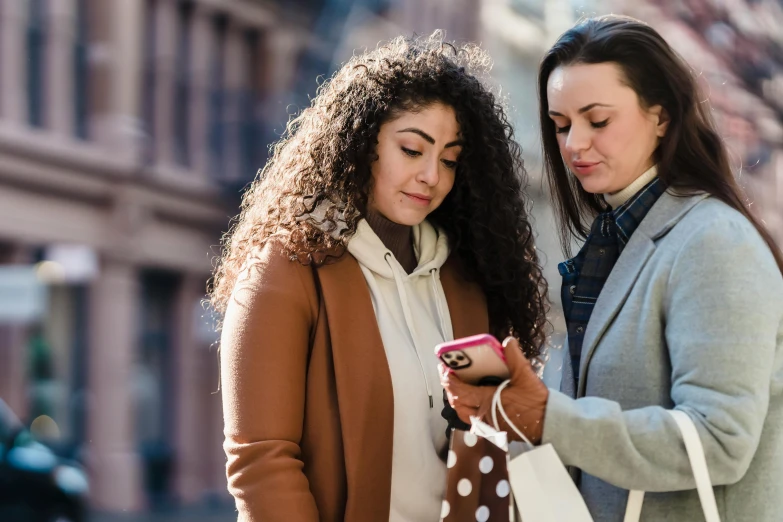 a couple of women standing next to each other on a street, trending on pexels, renaissance, scanning items with smartphone, avatar image, brown, promotional image