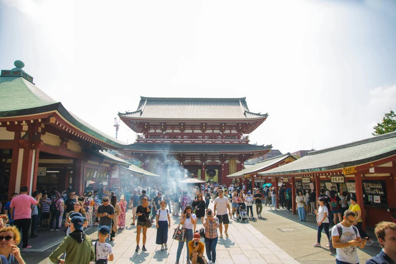 a group of people standing in front of a building, inspired by Itō Jakuchū, trending on unsplash, crowded square, 🚿🗝📝, temple fair, incense smoke fills the air