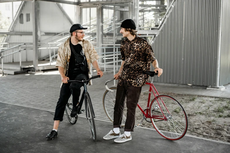 a couple of men standing next to each other with bikes, by Nina Hamnett, pexels contest winner, red shirt brown pants, streetwear, federation clothing, 2 animals