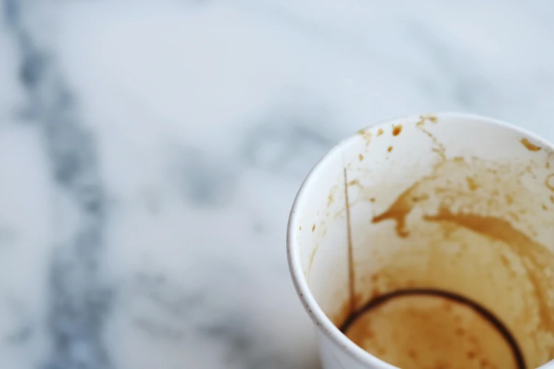 a close up of a cup of coffee on a table, unsplash, excrement, deteriorated, white marble interior photograph, caramel