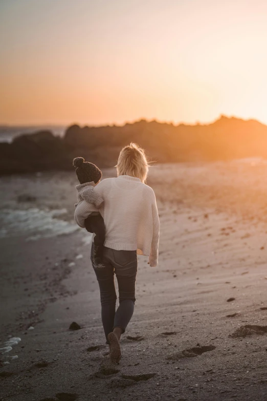 a woman carrying a child on the beach at sunset, by Jesper Knudsen, unsplash, minimalism, rhode island, beautiful natural soft light, casually dressed, beautiful boy