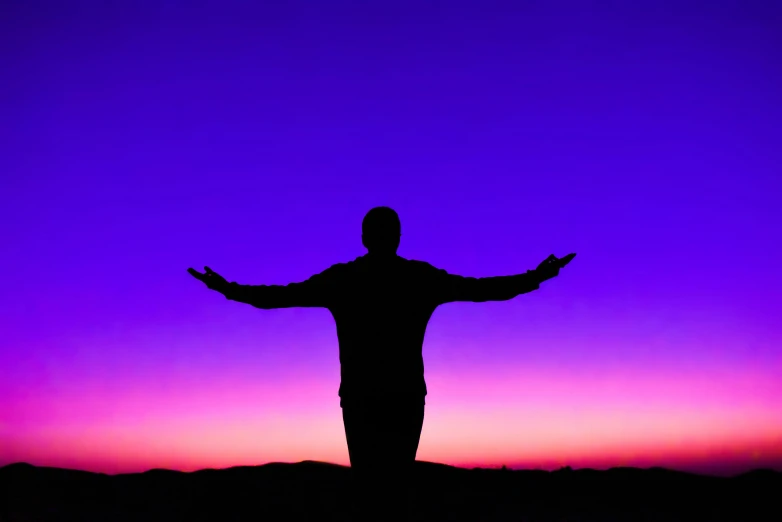 a man standing on top of a hill at sunset, an album cover, pexels, symbolism, purple and blue neons, arms open, prayer, purple blue color scheme